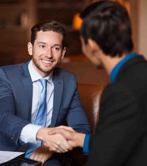 Closeup of two smiling business men shaking hands in cafe. One man is sitting back to camera.
